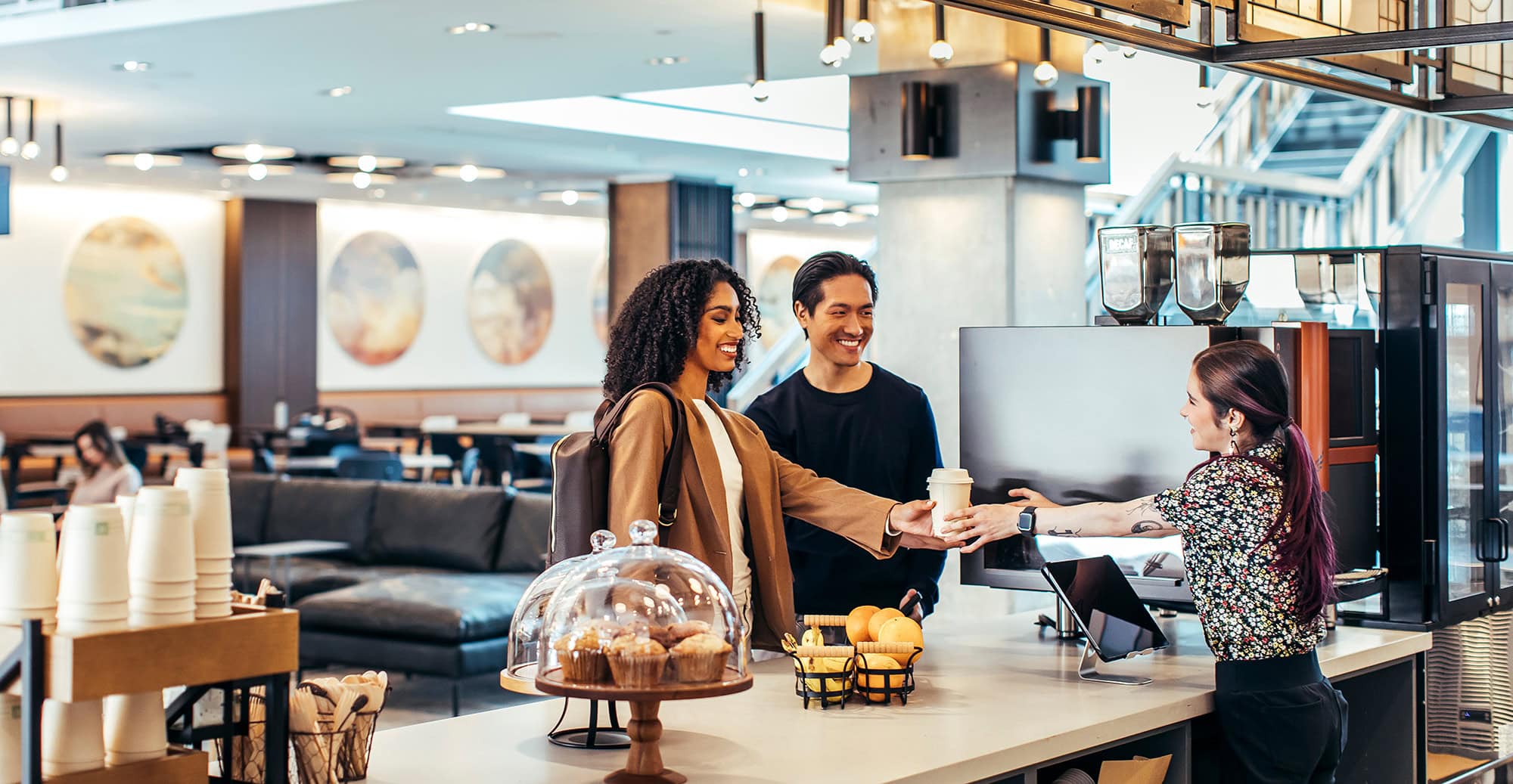 Barista handing a coffee to a smiling customer in modern coffee shop with stylish decor
