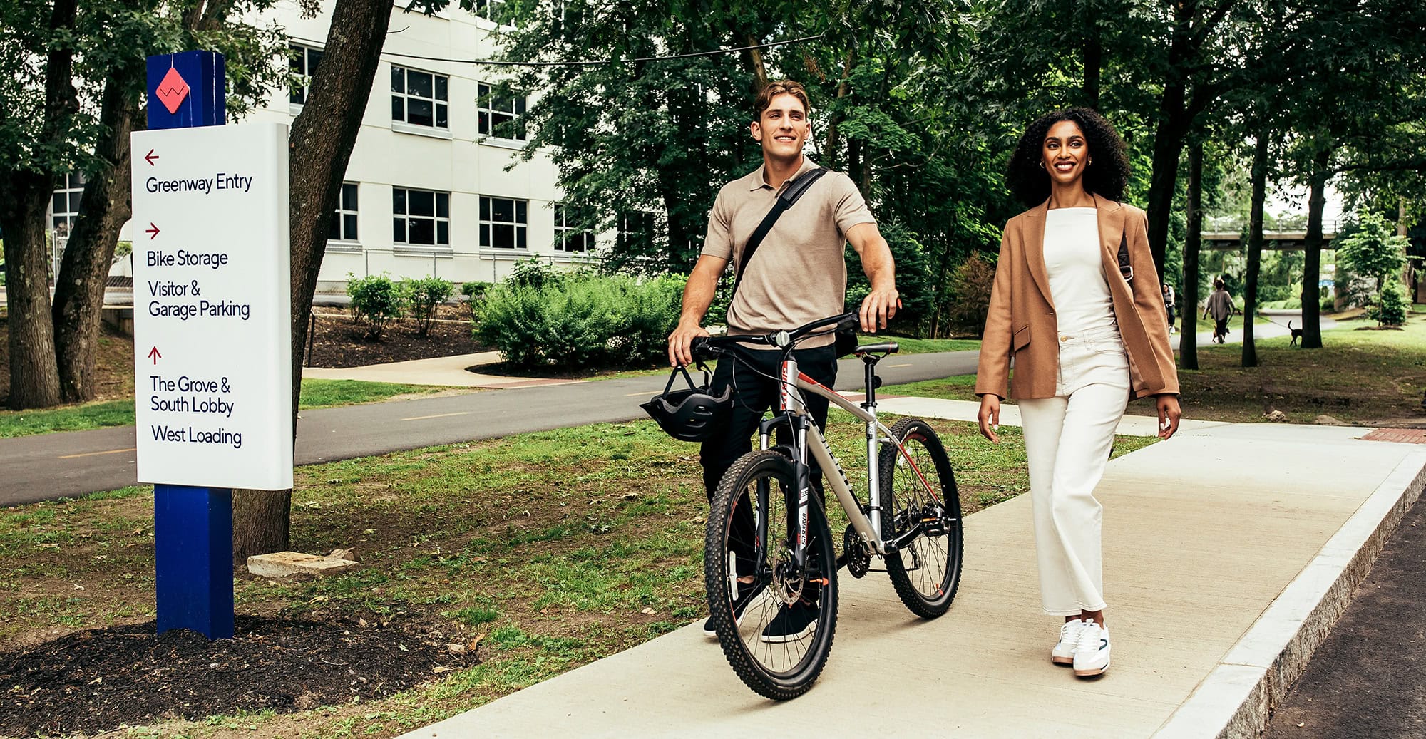 Two colleagues walk along a tree-lined path, enjoying a break around a corporate campus